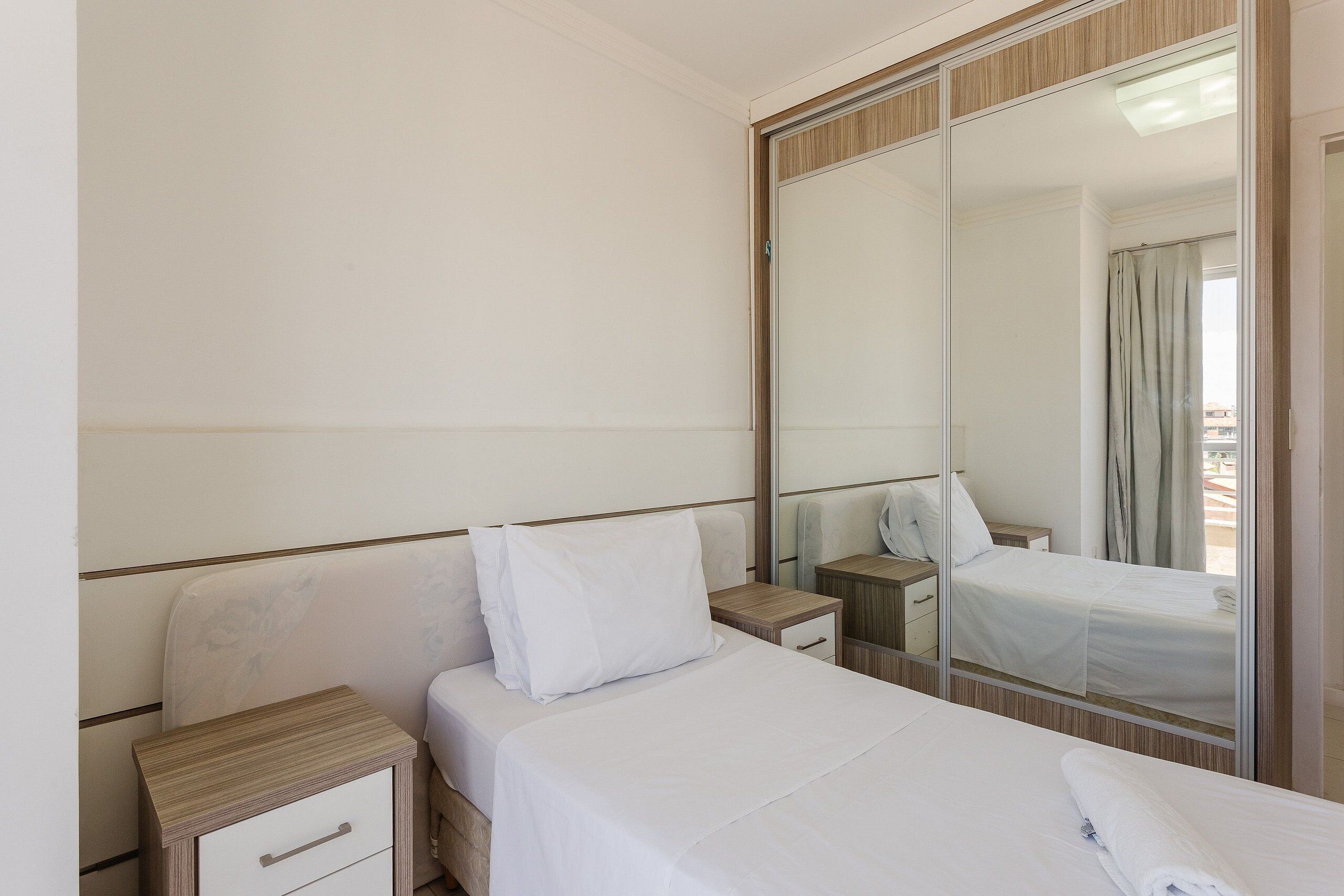 Habitación de hotel con cama, mesita de noche, espejo y armario.