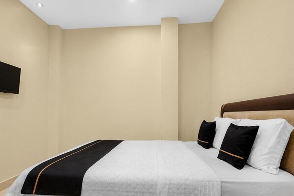 A hotel room with a bed, a flat-screen TV mounted on the wall, and a brown headboard.