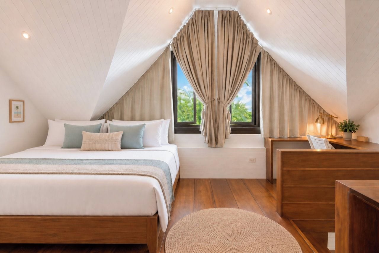 Quarto com cama, escrivaninha, janela com cortinas e vista para o verde lá fora.