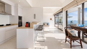 Una cocina moderna con una isla central, un comedor con vistas y un amplio ventanal al mar.