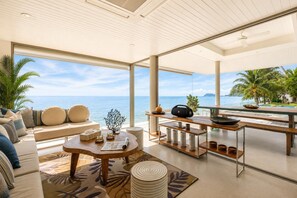 A spacious living area with a large window overlooking the sea, a comfortable seating area, and a wooden coffee table. - Villa de Sunset (Chang Wat Surat Thani)