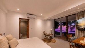 Habitación de hotel con cama, una silla, una mesa y un televisor mostrando una playa.