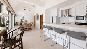Una cocina moderna con armarios blancos, una barra con taburetes y un comedor con mesa y sillas de madera.