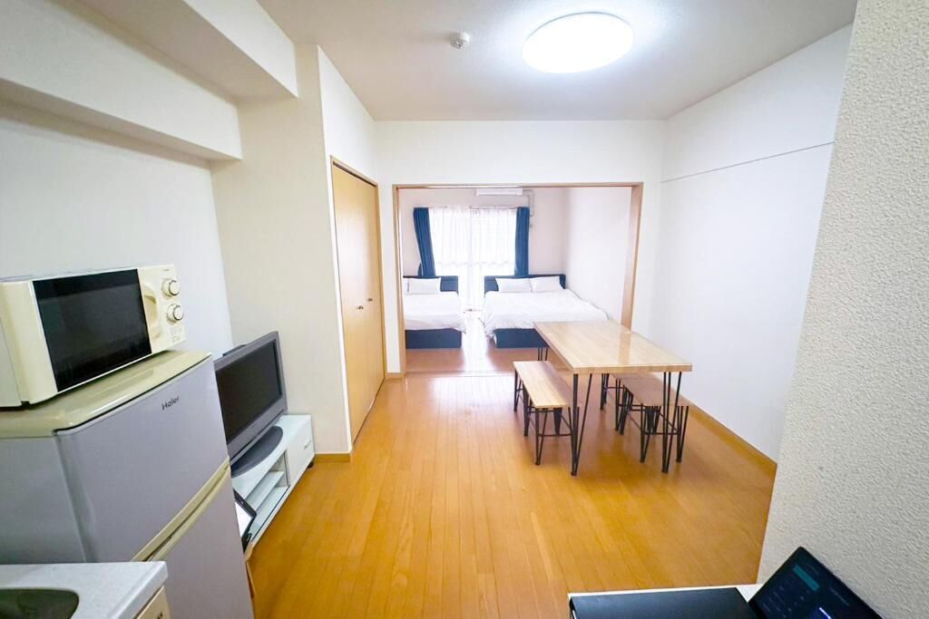 Habitación de hotel compacta con kitchenette, una cama individual, una mesita pequeña y un banco.