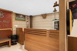 A reception desk with a wooden finish, a black leather chair, and a wall-mounted telephone. - Hotel O Kosta Living - Standard Single (Palembang)