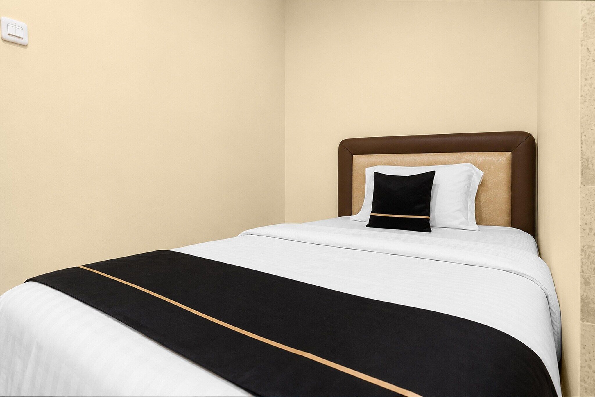 A single bed with a headboard, a white and black bedspread, and a single pillow.
