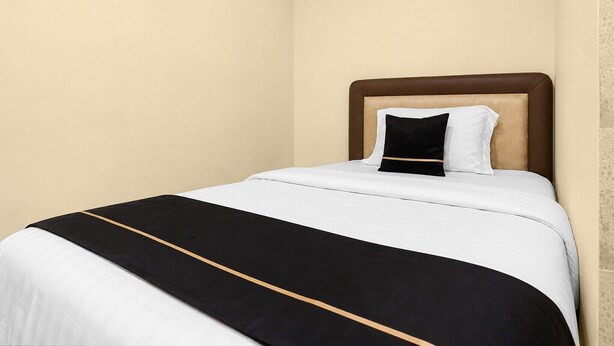 A single bed with a headboard, a white and black bedspread, and a single pillow. - Hotel O Kosta Living - Standard Single (Palembang)