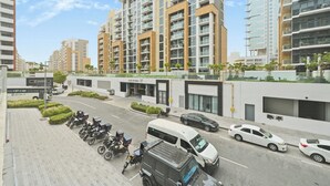 A modern building with multiple floors, a parking area with motorcycles and cars, and a clear sky. - Bloomfields 2BR in Azizi Riviera 43 (Dubai)