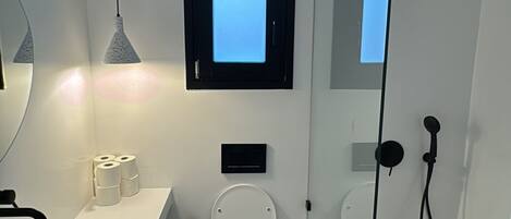 Ein modernes Badezimmer mit Waschbecken, Toilette und Dusche. Über der Toilette befindet sich ein Fenster, an der Wand ein Spiegel und eine Handtuchstange.