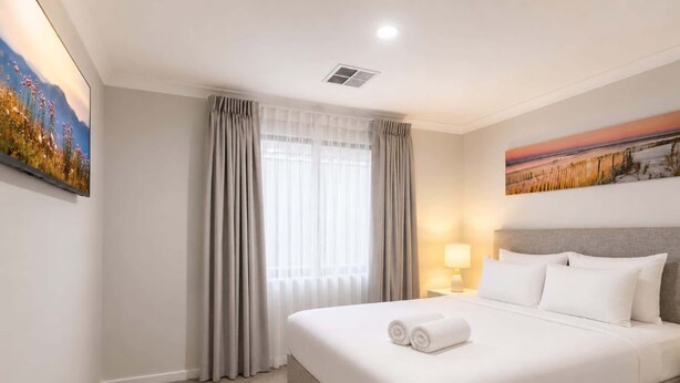 Quarto de hotel com uma cama grande, janela com cortinas, um quadro na parede e iluminação no teto.