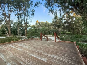 Eine Holzterrasse mit Metallgeländer, umgeben von Bäumen und Sträuchern.