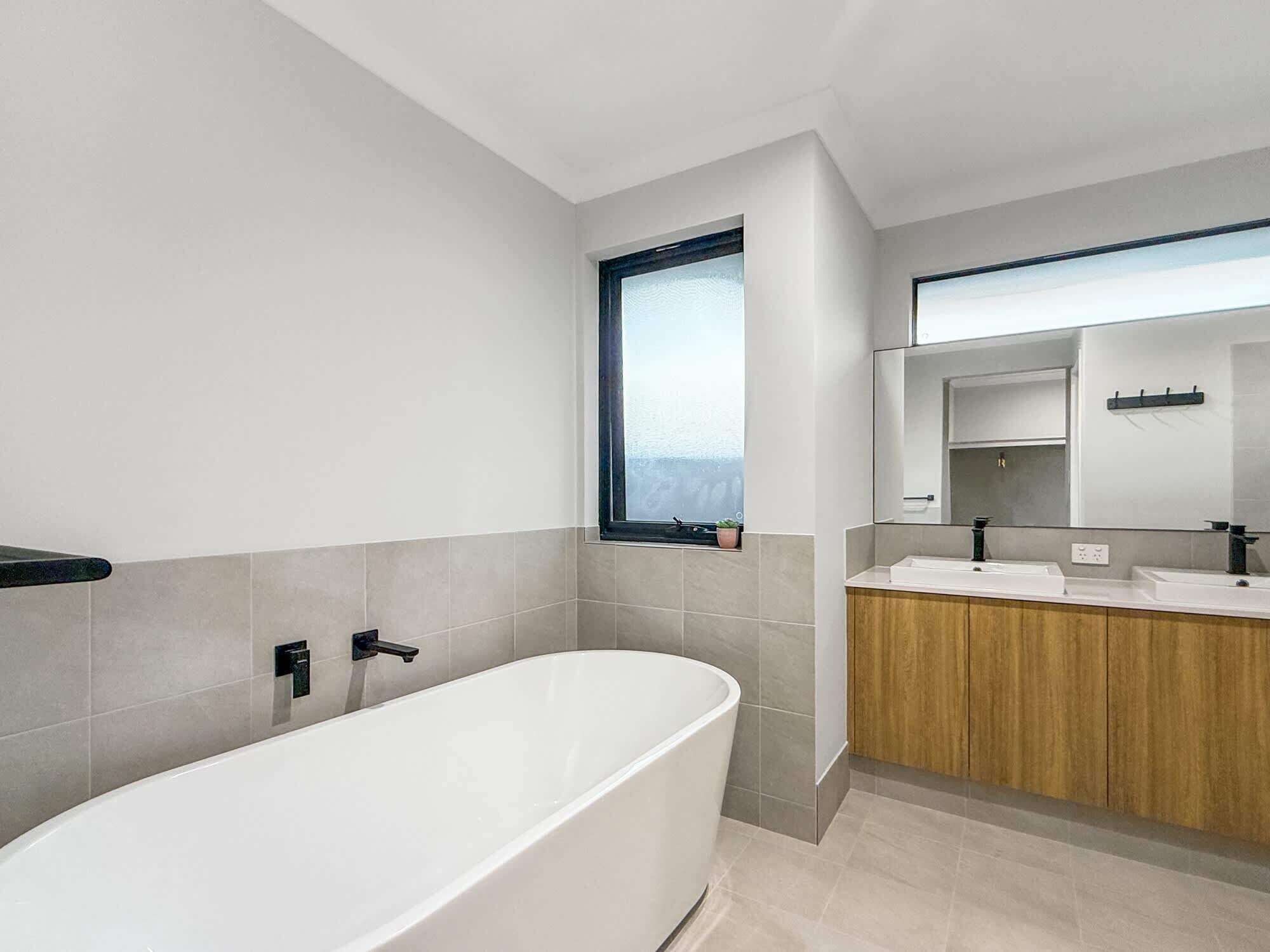 Ein modernes Badezimmer mit einer freistehenden Badewanne, einem Holzbadezimmer-Möbel und einem großen Spiegel.