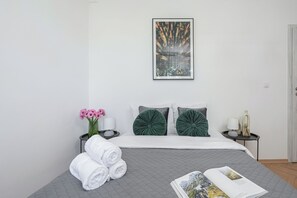 A modern bedroom with a bed, pillows, a bedside table with a lamp, a vase with flowers, and a framed picture on the wall. - Lumina 3-room Apart near Park & Balcony (Warszawa)