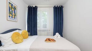 Un dormitorio con una cama, dos almohadas, una ventana con cortinas y un cuadro colgado en la pared.