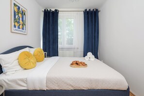 Quarto com cama, duas almofadas, janela com cortinas e um quadro na parede.