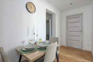 Uma área de refeições com uma mesa de madeira posta para dois, duas velas e dois copos de vinho branco.