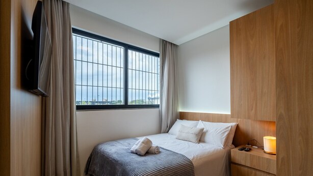 Ein Hotelzimmer mit Bett, Nachttisch, Lampe und einem an der Wand befestigten Fernseher.