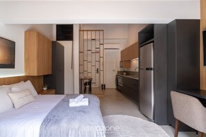 Ein modernes Hotelzimmer mit einem ordentlich bezogenen Bett, einer kleinen Küchenzeile und einer Sitzecke.