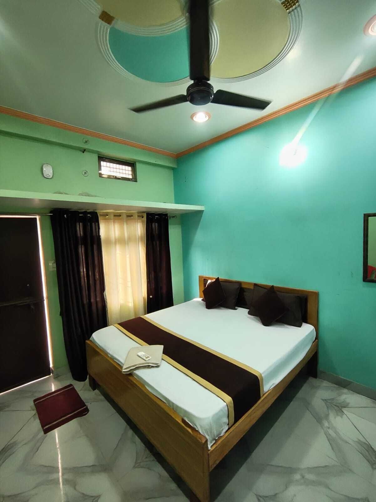 Una habitación con cama, ventilador de techo, lámpara, puerta y ventana con cortinas.