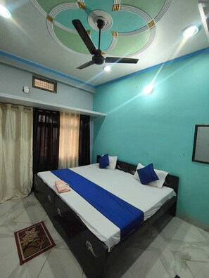 A bedroom with a bed, curtains, a ceiling fan, and a window with curtains. - Shri Janki Raman Kunj Ram Mandir (Ayodhya)