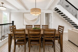Ein Essbereich mit Holztisch und Stühlen, einer Pendelleuchte und einer Treppe mit schwarzer Geländer.