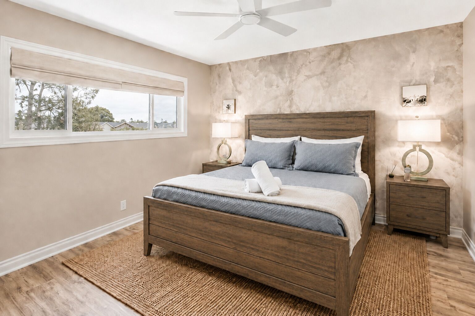 Une chambre à coucher avec un lit, deux tables de chevet, un ventilateur de plafond et une fenêtre.