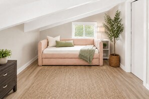 A cozy loft bedroom with a high ceiling, a beige sofa, a small side table, a potted plant, and a window with blinds. - NEW Huge Family Beach House in Silver Strand (Oxnard)