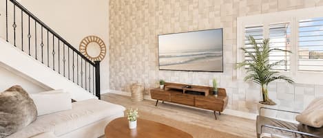 Una sala de estar moderna con una escalera, un televisor de pantalla plana, una mesa de centro de madera y una planta grande en maceta.