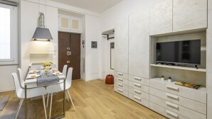 Een moderne keuken met witte kastjes, een eettafel voor vier personen en een flatscreen aan de muur.