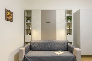 A room with a grey sofa, a bookshelf, and a door. - Sabotino, 16 – Milan Vibes (Milano)