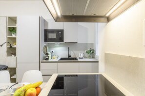 A modern kitchen with a built-in microwave, a kettle, and a sink. There is a dining table with fruits and a coffee cup. - Sabotino, 16 – Milan Vibes (Milano)