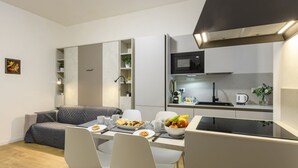Een ruimtelijk ingerichte leefruimte met kitchenette, eethoek en een bank.