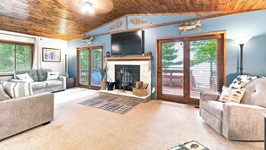 A cozy living room with a fireplace, a flat-screen TV, and a large window.