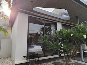 Ein modernes Haus mit einem großen Glasfenster, einer kleinen Pflanzenterrasse und einer Holzbalkendecke.