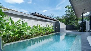 Un área de piscina moderna con una piscina cristalina, rodeada de abundante vegetación y una estructura de edificio contemporánea.