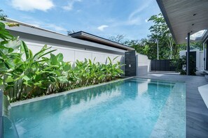 Ein moderner Poolbereich mit klarem Wasser, umgeben von üppiger Bepflanzung und einem zeitgemäßen Gebäudebau.