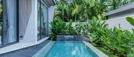 Une piscine rectangulaire agrémentée d’une cascade, entourée d’une végétation tropicale luxuriante et bordée d’une architecture moderne.