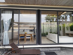 Ein modernes Interieur mit Essbereich, einer Couch und einer großen Schiebeglastür, die auf einen Balkon mit Pflanzen führt.