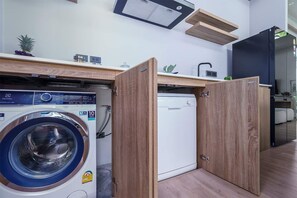 Ein kleiner Waschraum mit Waschmaschine und Trockner, Holzschränken und einer Arbeitsplatte mit Spüle und Dekorationselementen.