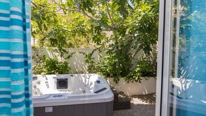 Een hottub in een achtertuin met een witte muur en een boom.