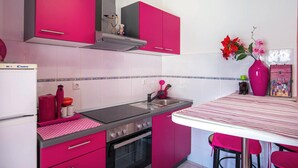 Een keuken met roze kastjes, een fornuis, een oven en een spoelbak.