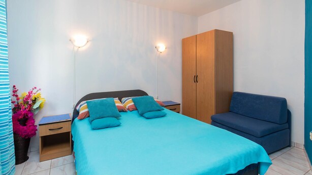 Een slaapkamer met een bed, een kledingkast, een nachtkastje en een blauwe bank.
