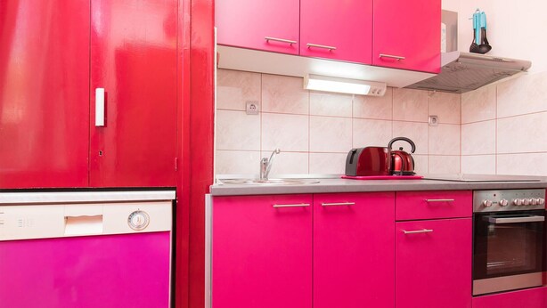 Une cuisine avec des meubles de rangement rouges, un évier en acier inoxydable, une bouilloire et une cuisinière.