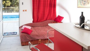 Een slaapkamer met een bed, een rode stoel, een klein tafeltje met een fles en glas, en uitzicht op een zwembad.