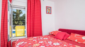 Een slaapkamer met een bed, rode gordijnen, een raam en een gele stoel ernaast.
