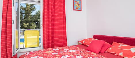 A bedroom with a bed, red curtains, a window, and a yellow chair outside.