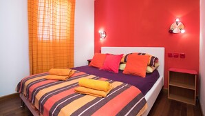 Ein Bett mit gestreifter Bettwäsche, orangefarbenen Kissen und aufgerollten Handtüchern.