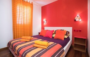 Ein Bett mit gestreifter Bettwäsche, orangefarbenen Kissen und aufgerollten Handtüchern.