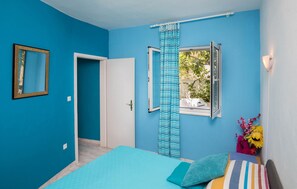 Une pièce avec un lit, une fenêtre avec des rideaux, une porte et un miroir au mur.