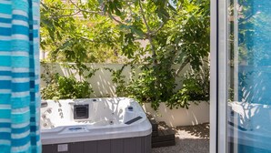 Ein Whirlpool in einem Garten mit Baum und weißer Wand im Hintergrund.